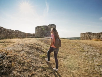 Ruine Falkenburg Eine Frau mit Rucksack geht bei sonnigem Wetter auf einen Hügel zur Ruine Falkenburg.