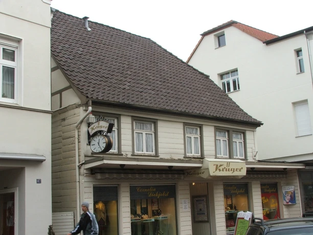 Fachwerkhaus mit Ziegeldach und markanter Uhr; im Erdgeschoss ein Friseurgeschäft mit Schaufenstern.