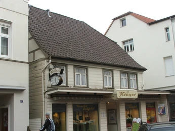 Lange Straße 89 Fachwerkhaus mit Ziegeldach und markanter Uhr; im Erdgeschoss ein Friseurgeschäft mit Schaufenstern.