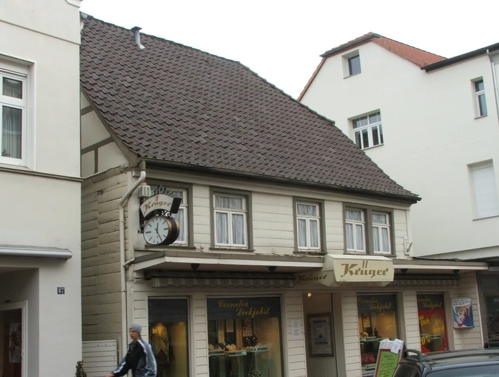 Lange Straße 89 Fachwerkhaus mit Ziegeldach und markanter Uhr; im Erdgeschoss ein Friseurgeschäft mit Schaufenstern.