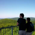 Die Aussicht genießen Zwei Personen betrachten von einer Aussichtsplattform aus die weiten, bewaldeten Hügel einer Landschaft.