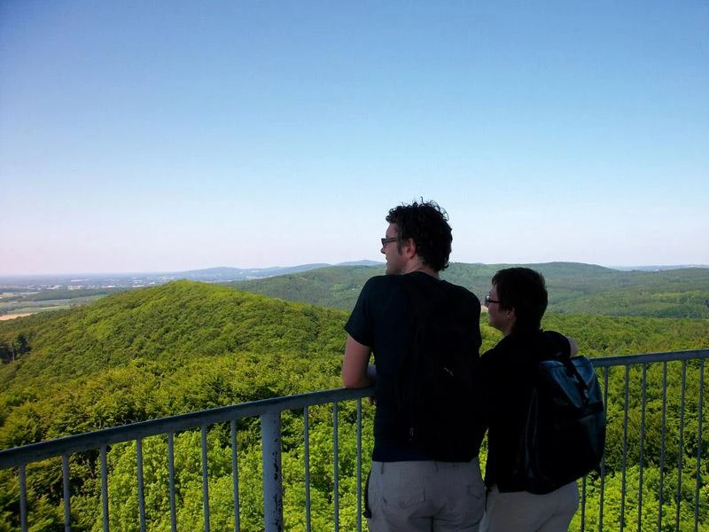 Die Aussicht genießen Zwei Personen betrachten von einer Aussichtsplattform aus die weiten, bewaldeten Hügel einer Landschaft.