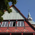 Fachwerkhaus mit bunten Ornamenten, im Hintergrund Kirchturm unter blauem Himmel sichtbar.