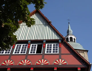 Historisches Fachwerkhaus in Wiedenbrück Fachwerkhaus mit bunten Ornamenten, im Hintergrund Kirchturm unter blauem Himmel sichtbar.