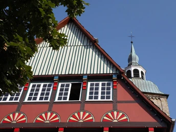 Historisches Fachwerkhaus in Wiedenbrück Fachwerkhaus mit bunten Ornamenten, im Hintergrund Kirchturm unter blauem Himmel sichtbar.