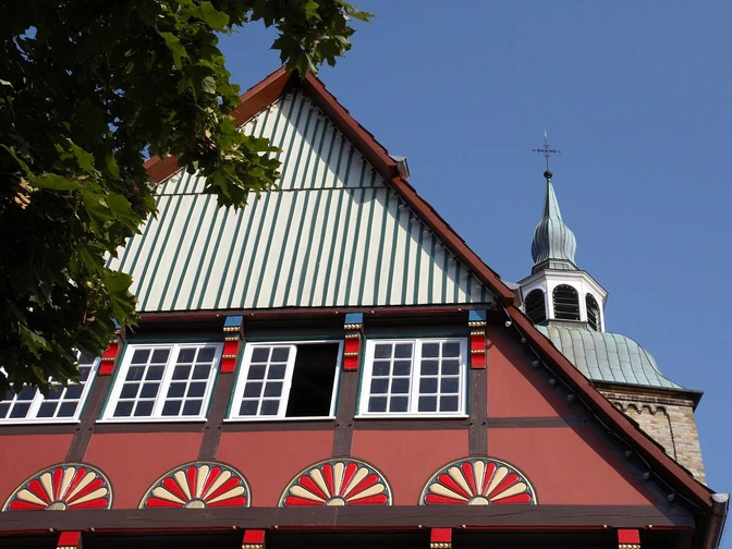 Historisches Fachwerkhaus in Wiedenbrück Fachwerkhaus mit bunten Ornamenten, im Hintergrund Kirchturm unter blauem Himmel sichtbar.