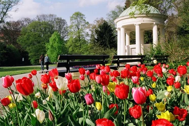 Leopoldsprudel Bunter Tulpenbeet in einem gepflegten Park mit klassizistischem Pavillon und Paar beim Spaziergang.