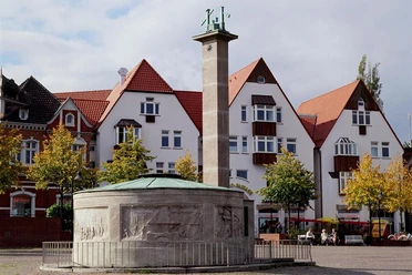 Paulinenquelle Historischer Brunnen auf einem Platz mit umliegenden Fachwerkhäusern vor bewölktem Himmel.