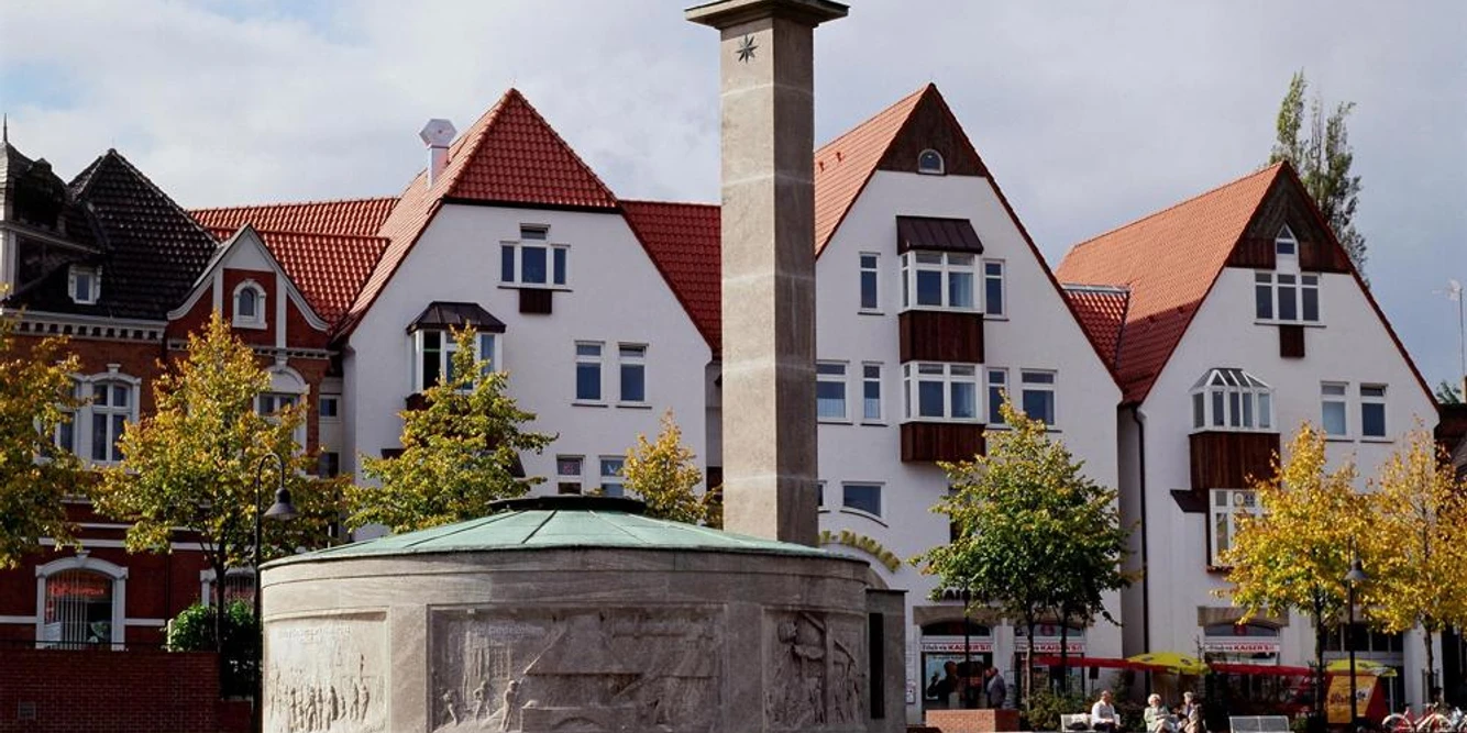 Paulinenquelle Historischer Brunnen auf einem Platz mit umliegenden Fachwerkhäusern vor bewölktem Himmel.