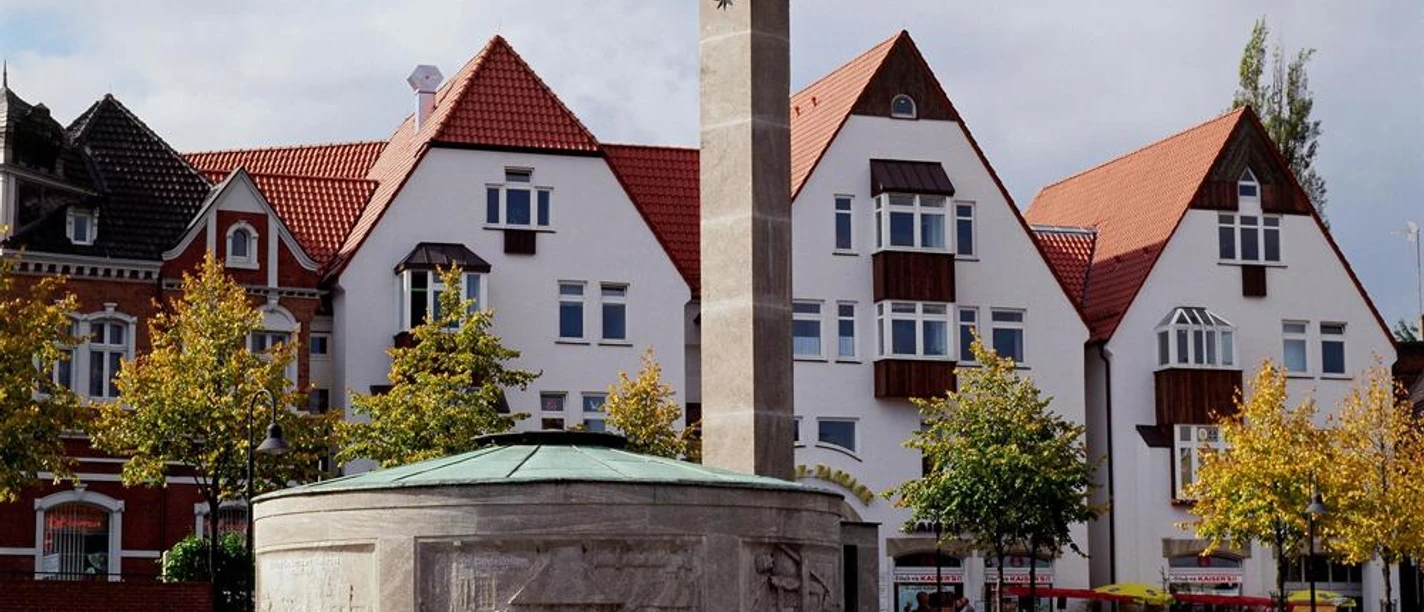 Paulinenquelle Historischer Brunnen auf einem Platz mit umliegenden Fachwerkhäusern vor bewölktem Himmel.