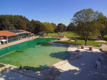freibad-versmold-opt Freibad mit großem Schwimmbecken, umliegenden Liegewiesen und einem Spielplatz im Hintergrund.