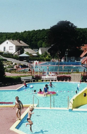 Waldschwimmbad Preußisch Oldendorf Kinderbecken mit Rutsche und Wasserspielen vor einem Waldschwimmbad an einem sonnigen Tag.