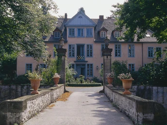 Historisches Herrenhaus mit gelber Fassade, symmetrischen Fenstern und Natursteinsäulen vor dem Eingang.