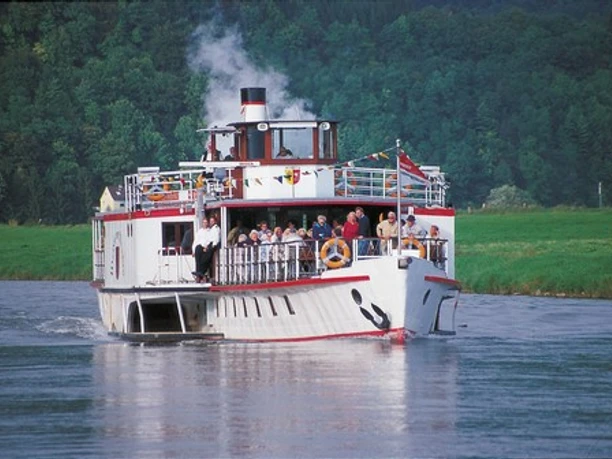 Wappen von Minden Ein Dampfschiff mit Ausflugsgästen fährt auf einem Fluss, umgeben von Wäldern und grüner Landschaft.