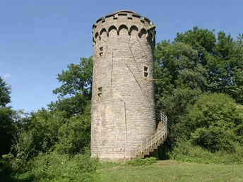 Holsterturm Wahrzeichen der Stadt Steinerner Turm inmitten grüner Vegetation, mit Wendeltreppe und markanten Zinnen am oberen Rand.