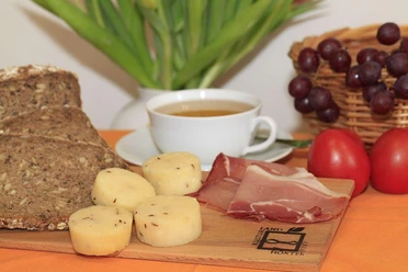 Brot, Käse und Schinken - Leckereien aus Nieheim Brot, Käse mit Kümmel und Schinken auf Holzbrett, begleitet von Kaffeetasse und Trauben.