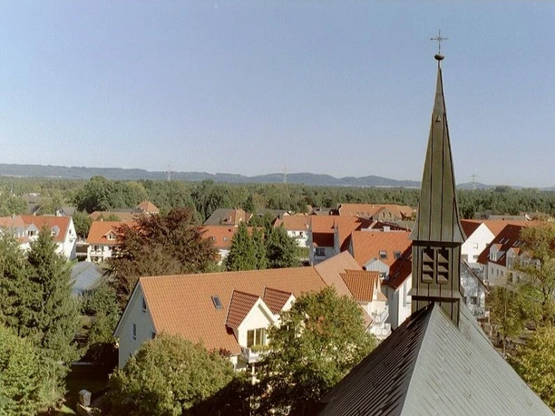 Kath. Kirche St. Ursula 1 Kirchturmspitze von St. Ursula inmitten eines Wohngebiets mit roten Dächern und umgebender Natur.