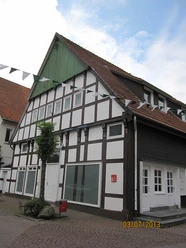 Fachwerkhaus mit weißen Wänden, dunkelbraunen Balken, Sprossenfenstern und geschmücktem Giebel.