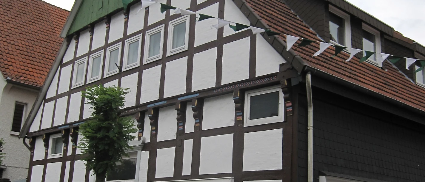 Fachwerkhaus mit weißen Wänden, dunkelbraunen Balken, Sprossenfenstern und geschmücktem Giebel.
