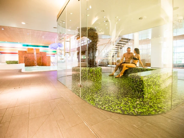 Ein modernes Paar sitzt entspannt in der durchsichtigen Sole-Dampfsauna der Vitasol Therme.