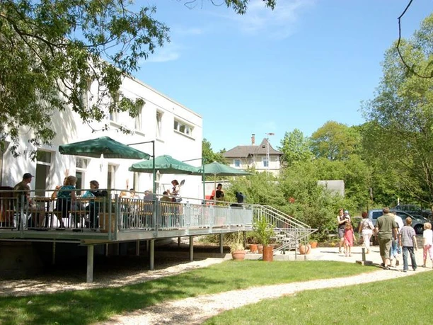 Menschen genießen sonnige Stunden auf einer überdachten Terrasse eines Seminarhauses im Grünen.