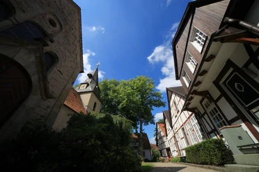 Dorfkern Bockhorst Fachwerkhäuser und ein Kirchturm ragen unter einem blauen Himmel mit weißen Wolken und grünen Bäumen hervor.