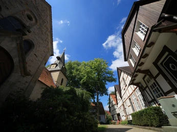 Dorfkern Bockhorst Fachwerkhäuser und ein Kirchturm ragen unter einem blauen Himmel mit weißen Wolken und grünen Bäumen hervor.