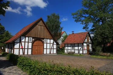 Bockhorster Kotten & Backhaus Fachwerkhäuser unter blauem Himmel mit Ziegeln gedeckt, umgeben von grünen Bäumen und Hecken.