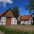 Bockhorster Kotten & Backhaus Fachwerkhäuser unter blauem Himmel mit Ziegeln gedeckt, umgeben von grünen Bäumen und Hecken.