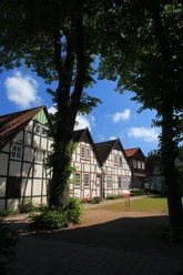 Dorfkern Bockhorst Traditionelle Fachwerkhäuser in einer Baumallee, Himmel mit wenigen Wolken im Hintergrund.
