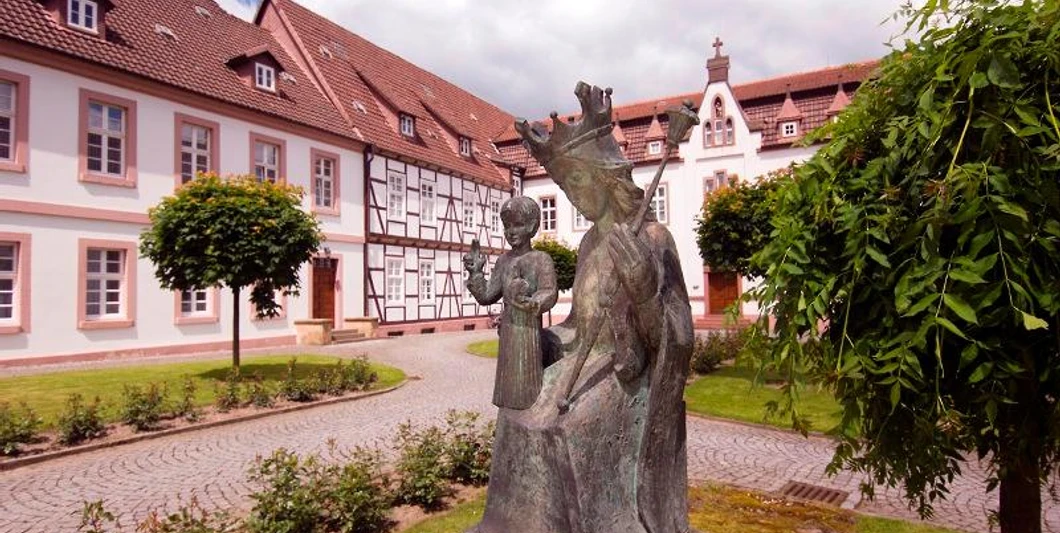 Bronzestatue im Vordergrund vor einem historischen Klostergebäude mit Fachwerk und rotem Dach.