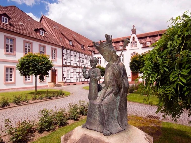Bronzestatue im Vordergrund vor einem historischen Klostergebäude mit Fachwerk und rotem Dach.