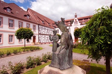 Kloster auf der Brede, Brakel Bronzestatue im Vordergrund vor einem historischen Klostergebäude mit Fachwerk und rotem Dach.