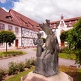 Kloster auf der Brede, Brakel Bronzestatue im Vordergrund vor einem historischen Klostergebäude mit Fachwerk und rotem Dach.