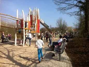 Wasserspielplatz und Kletterturm Kinder spielen fröhlich auf einem großen Spielplatz mit Klettergerüst und Rutsche, umgeben von Bäumen.