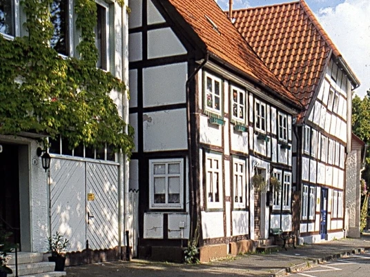 Am Pideritplatz Ein Ensemble traditioneller Fachwerkhäuser mit roten Ziegeldächern neben bunten Blumenbeeten.