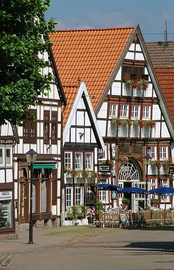 Fachwerkhäuser mit roten Dächern und Blumenkästen, eine Fußgängerzone mit einem Café im Freien.