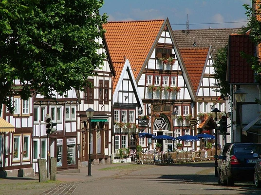 Fachwerkhäuser mit roten Dächern und Blumenkästen, eine Fußgängerzone mit einem Café im Freien.