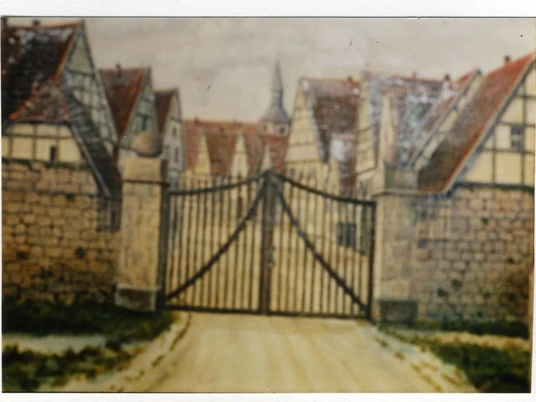 Historisches Stadttor mit Eisenzaun, umgeben von Fachwerkhäusern mit roten Ziegeldächern.