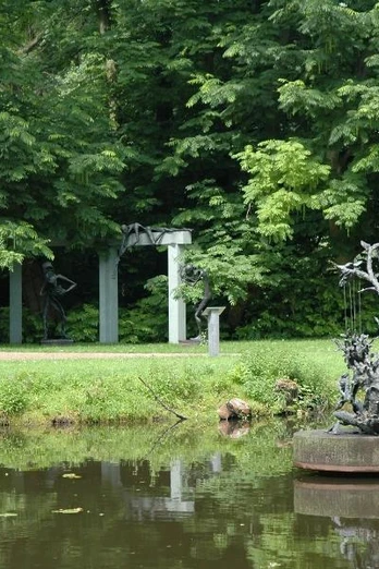 Klostergarten Rietberg - Skulpturenpark Wilfried Koch Bronzeskulptur auf Teich mit grünen Bäumen und einer Gartenlaube im Hintergrund.