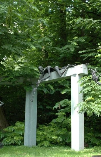 Skulpturen im Garten zeigen stilisierte menschliche Figuren aus Metall vor üppigem grünem Hintergrund.