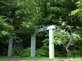 Klostergarten Rietberg - Skulpturenpark Wilfried Koch Skulpturen im Garten zeigen stilisierte menschliche Figuren aus Metall vor üppigem grünem Hintergrund.