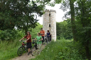 Radfahrergruppe passiert einen historischen Turm, umgeben von üppigem Grün im Sommer.