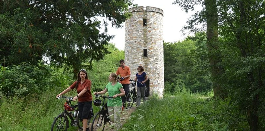 Lichtenturm (Haxter Warte) mit Radfahrern Radfahrergruppe passiert einen historischen Turm, umgeben von üppigem Grün im Sommer.