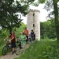 Lichtenturm (Haxter Warte) mit Radfahrern Radfahrergruppe passiert einen historischen Turm, umgeben von üppigem Grün im Sommer.