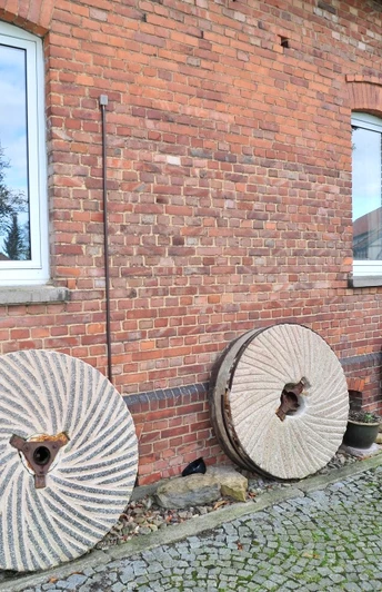 Hartingsche Mühle: Historische Mühlsteine an einer roten Backsteinfassade, Fenster, Kopfsteinpflaster.