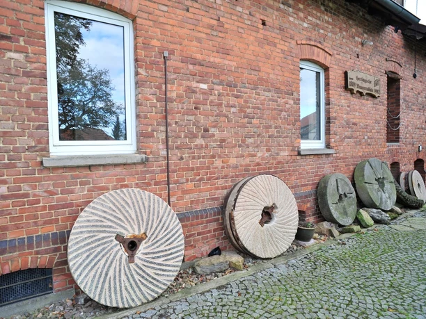 Hartingsche Mühle Hartingsche Mühle: Historische Mühlsteine an einer roten Backsteinfassade, Fenster, Kopfsteinpflaster.