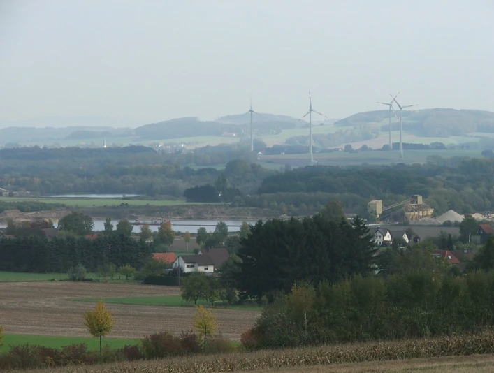 Blick zu den Kiesteichen Blick auf Kiesteiche mit umliegenden Feldern, Windrädern und sanften Hügeln im Hintergrund.