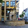 Liborius-Kump Brunnen mit Statue eines Heiligen vor einem modernen Gebäude; Fahrräder parken um den Brunnen.