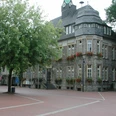 Historisches Rathaus mit grauer Steinfront, umgeben von Bäumen, roten Blumenkästen an den Fenstern.